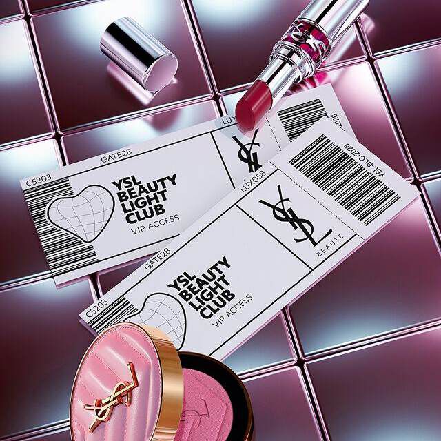 Produits de beaute YSL (rouge a levres et fard a joues) disposes avec des cartes d'acces VIP style billet sur une surface metallique reflechissante.