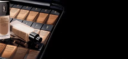 A collection of foundation bottles arranged neatly inside a black case, showcasing various shades of the product. The scene has a sleek, modern aesthetic with a dark background.
