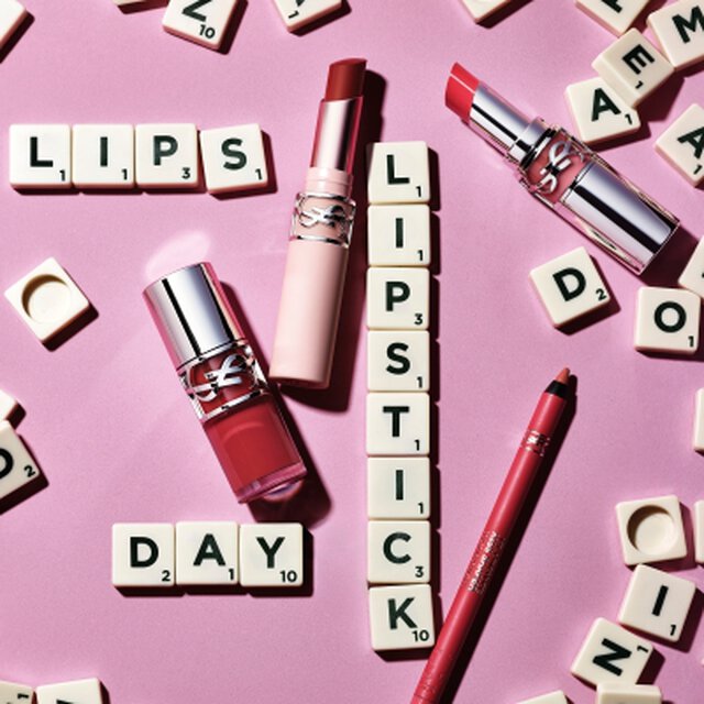 Rouges a levres YSL et crayon a levres disposes sur fond rose avec des lettres de Scrabble formant les mots "LIPS", "LIPSTICK" et "DAY"