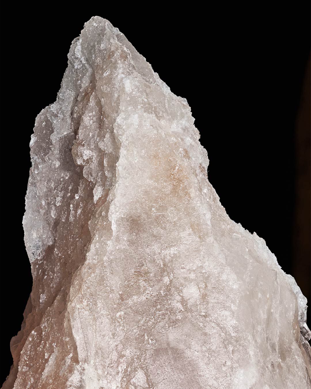 A close-up of a jagged, crystal-like formation with a pointed tip, illuminated against a dark background.