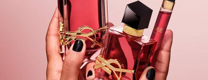 Mains tenant deux flacons de parfum YSL rouges et un vaporisateur de voyage