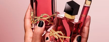 Mains tenant deux flacons de parfum YSL rouges et un vaporisateur de voyage