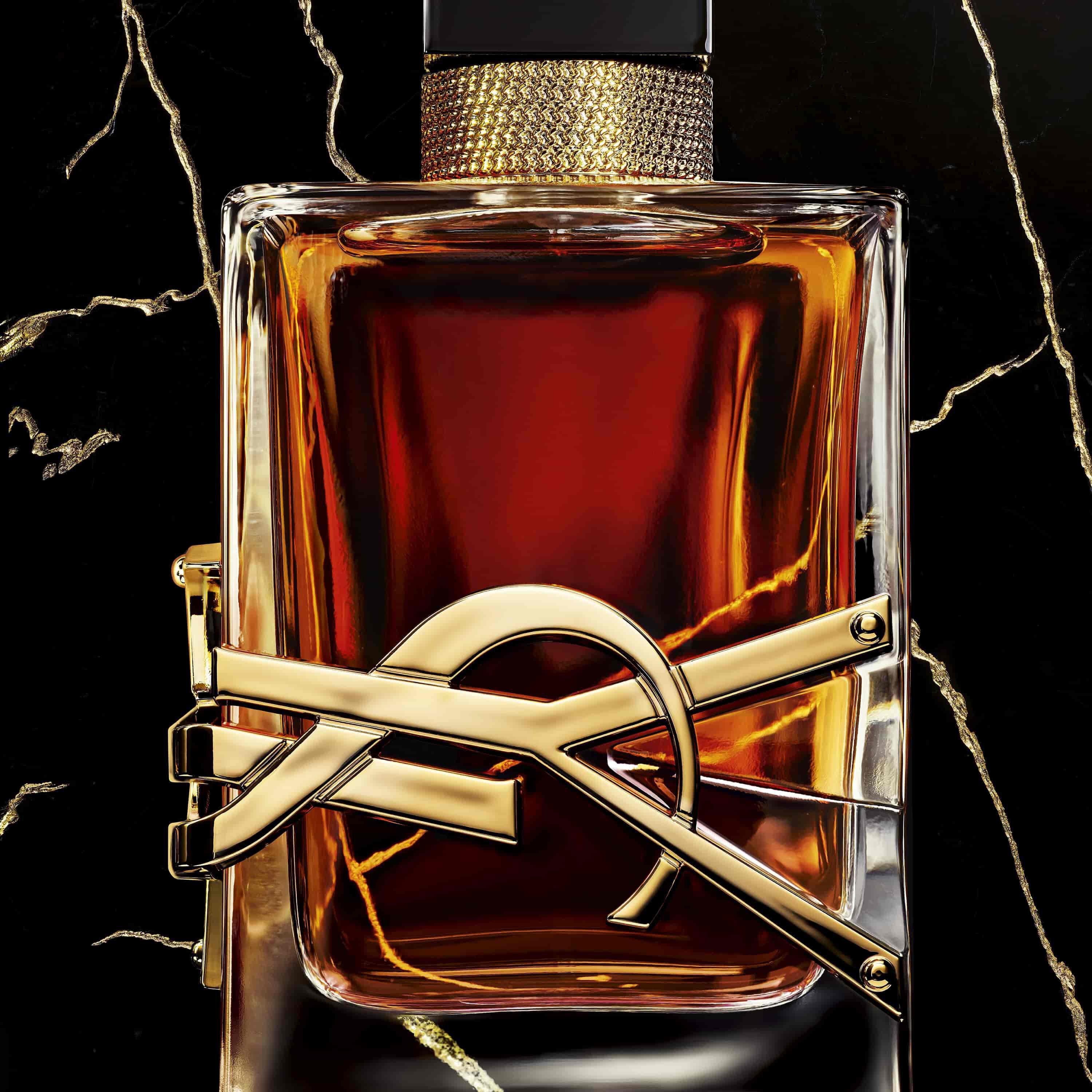 A close-up of a luxurious perfume bottle with a gold and black design, featuring a striking gold emblem and a dark, rich liquid inside, set against a dark, marbled background.