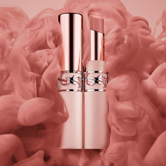 Un tube de rouge a levres argente Yves Saint Laurent avec le logo Cassandra, niche dans un lit de framboises fraiches et mures.