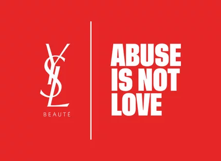 Logo YSL Beaute en blanc et le message "ABUSE IS NOT LOVE" en blanc, separes par une ligne verticale, sur un fond rouge vif.