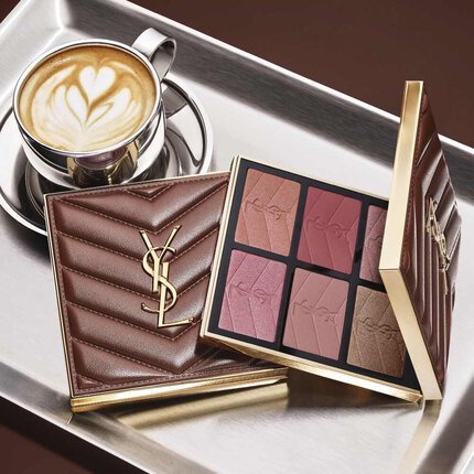 Palette de maquillage YSL et pochette matelassee a cote d’un cafe sur un plateau argente.