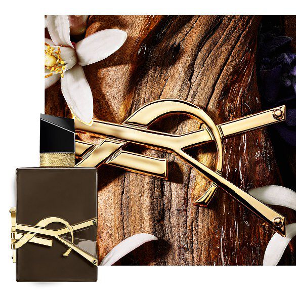 Flacon brun glace Libre Santal Couture sur ecorce de santal, orne de la Cassandre doree et de fleurs blanches.