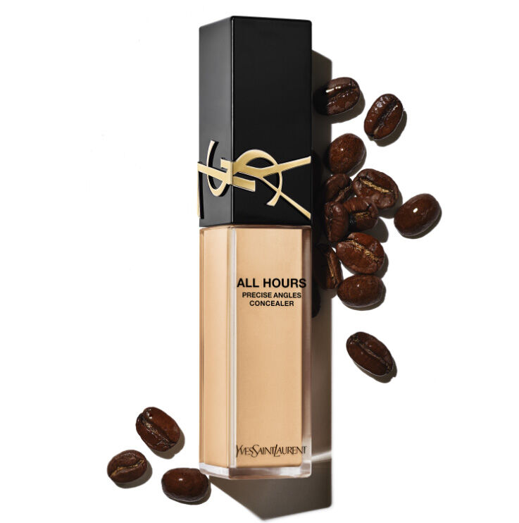 A bottle of Yves Saint Laurent All Hours Precise Angled Concealer in a beige shade, accompanied by scattered coffee beans against a white background.