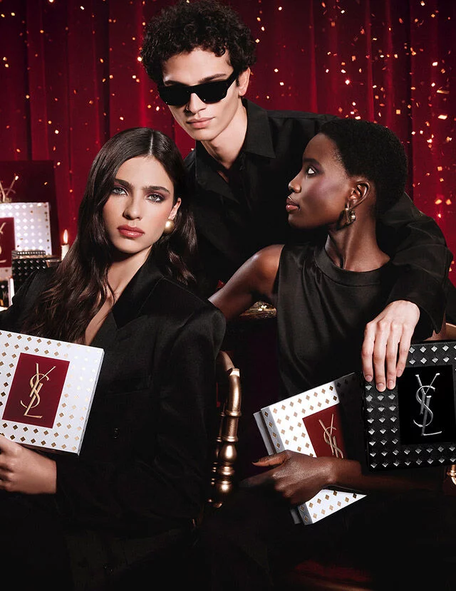 Models posing together holding luxury YSL Holiday gift boxes in a festive atmosphere.