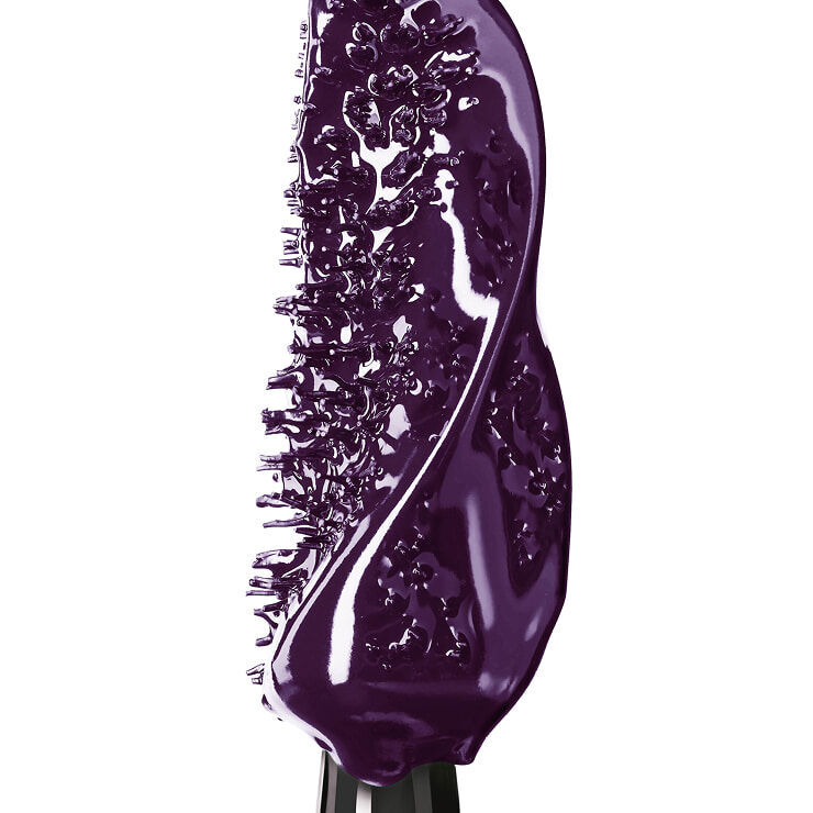 Gros plan extreme d'une brosse a mascara genereusement enduite d'une formule cremeuse et brillante violet fonce.