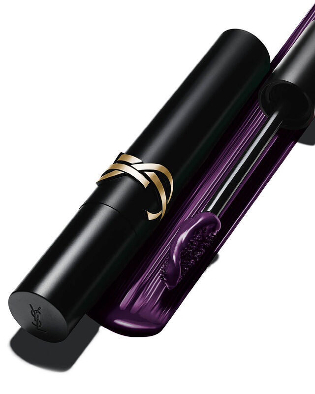 Gros plan d'un tube de mascara noir au logo dore a cote d'une brosse impregnee d'une formule violet fonce.