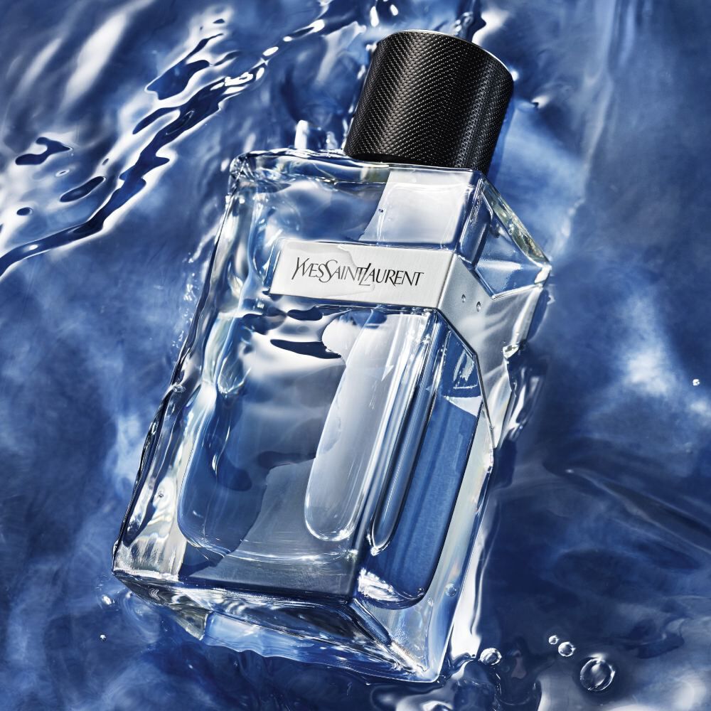 A clear glass bottle of Yves Saint Laurent fragrance submerged partially in blue water, reflecting light.