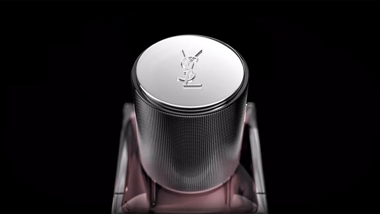 Vue rapprochee d'un bouchon de parfum texture argente avec le logo YSL en relief bien visible sur le dessus, sur un fond sombre.