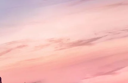 A perfume bottle with a black ribbon sits against a soft gradient sky at sunset, overlooking a cityscape.