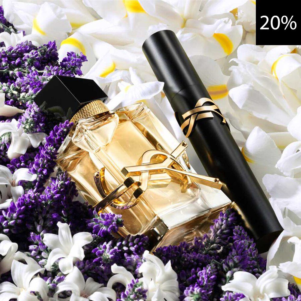 Un gros plan d'un elegant flacon de parfum YSL Libre et d'un mascara noir YSL, tous deux avec des accents dores, niches parmi de la lavande violette vibrante et de delicates fleurs blanches et jaunes. Un carre noir avec le texte blanc '20%' est visible en haut a droite, indiquant une reduction.
