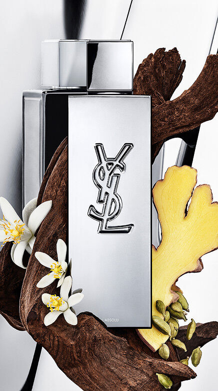 Flacon de parfum YSL Y L'ABSOLU entoure de bois fonce, de fleurs blanches de neroli, de gingembre et de gousses de cardamome.