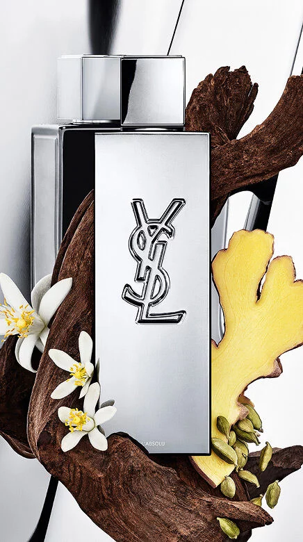 Flacon de parfum YSL Y L'ABSOLU entoure de bois fonce, de fleurs blanches de neroli, de gingembre et de gousses de cardamome.