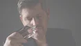 Un homme en haut sombre tient une bouteille de parfum a son nez, inhalant profondement son parfum.