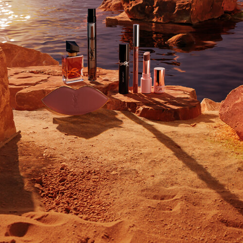 Maquillage, parfums YSL et trousse blanche dans un desert ensoleille.