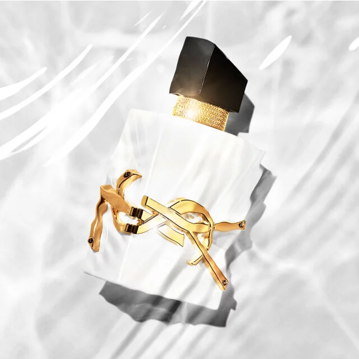 Flacon de parfum elegant avec un bouchon noir et une etiquette doree, pose sur une surface brillante evoquant l'eau.