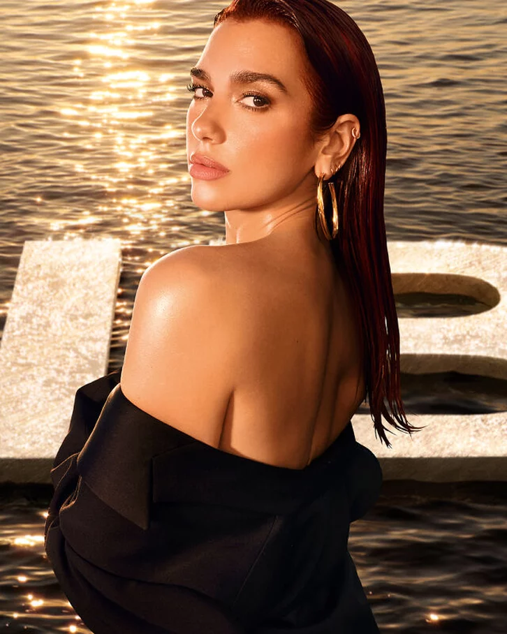 Femme elegante avec les cheveux longs, regardant vers l'objectif, devant un fond d'eau et le mot "LIBRE" en lettres geantes.