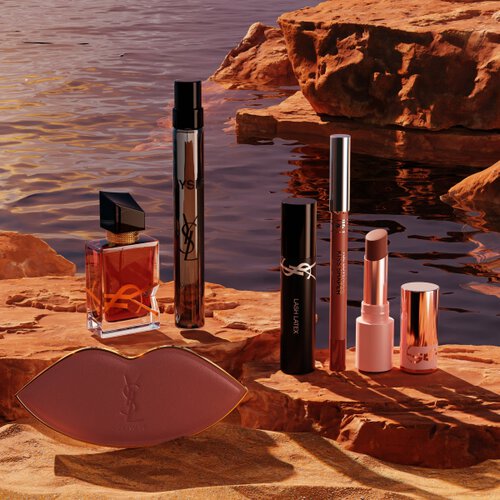 Maquillage, parfums YSL et trousse blanche dans un desert ensoleille.