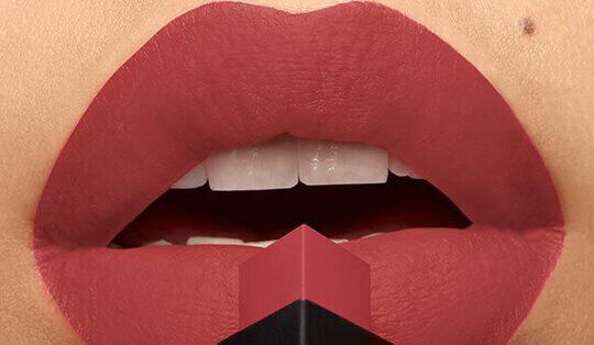 Close-up of red lips with a matte finish, featuring a lipstick bullet pointed towards them, showcasing a bold makeup look.