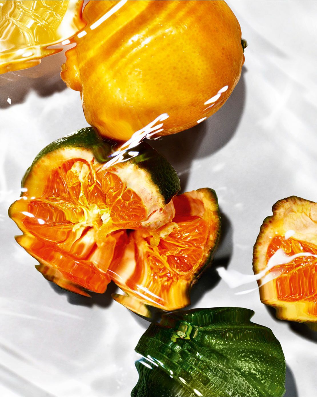 Alt text: A close-up of citrus fruits, including a whole lemon and sliced orange segments, partially submerged in clear water, with light reflections creating a dynamic and vibrant effect.