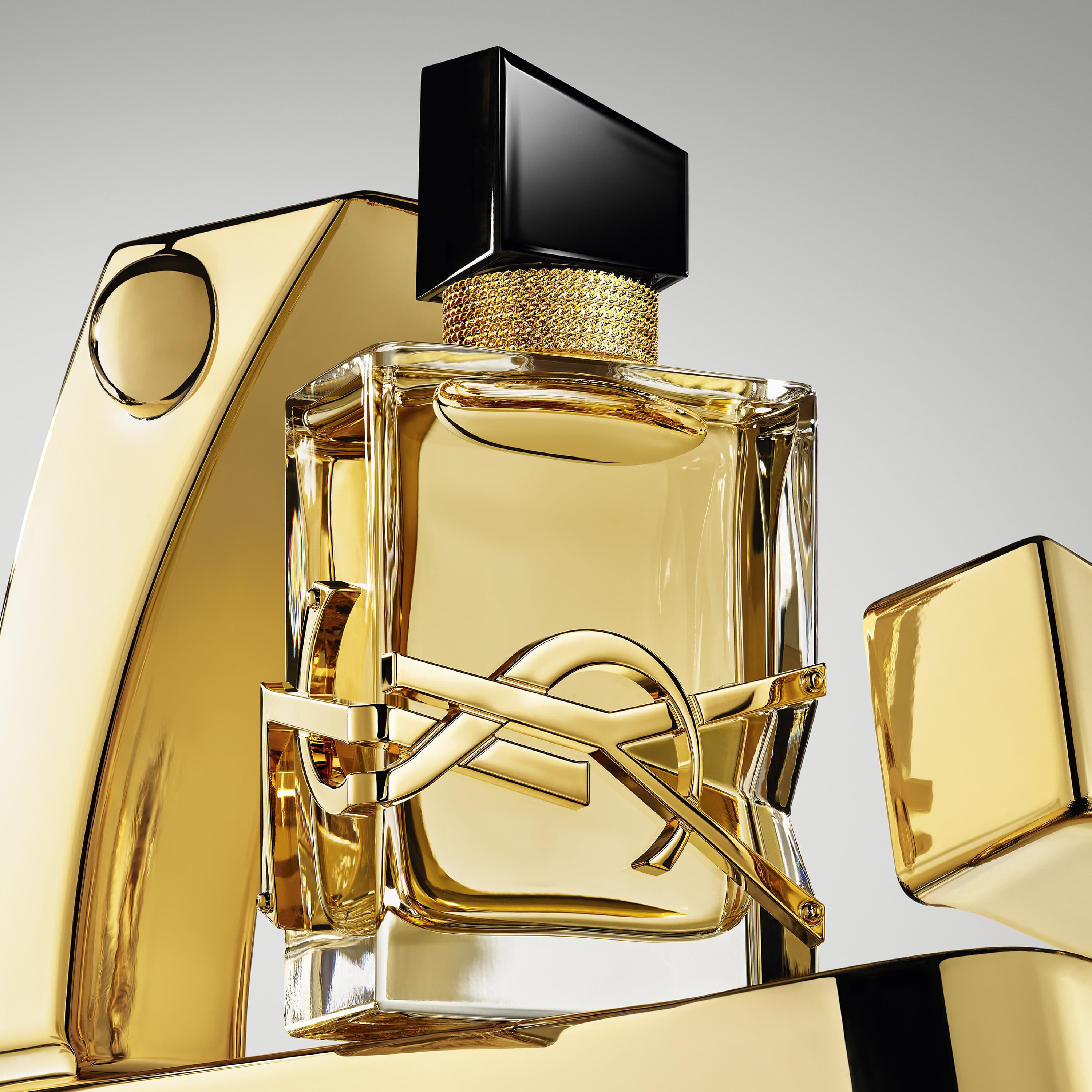 Flacon de parfum YSL dore, avec capuchon noir et logo, entoure d'elements dores.