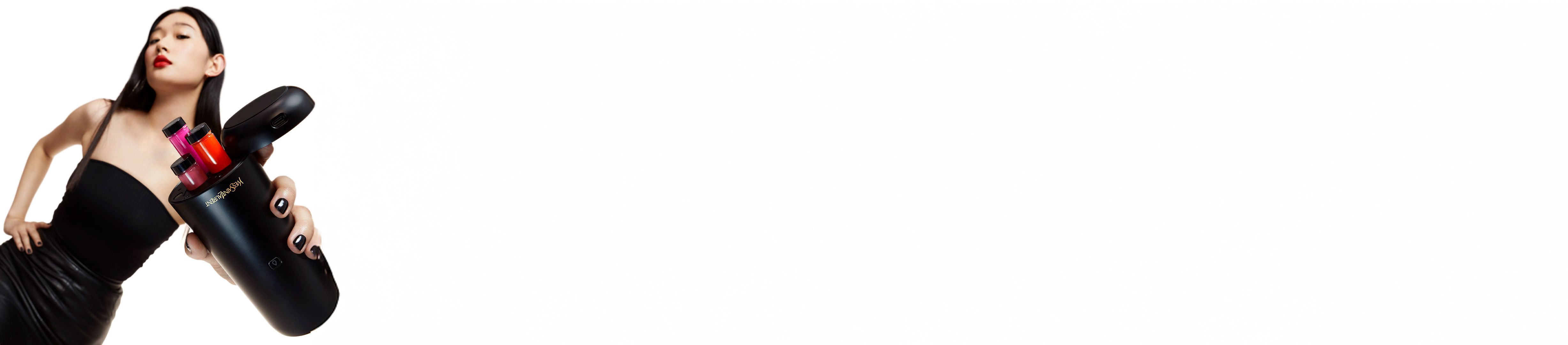 Une femme au rouge a levres rouge tenant un appareil de beaute noir Yves Saint Laurent avec des inserts cosmetiques colores.