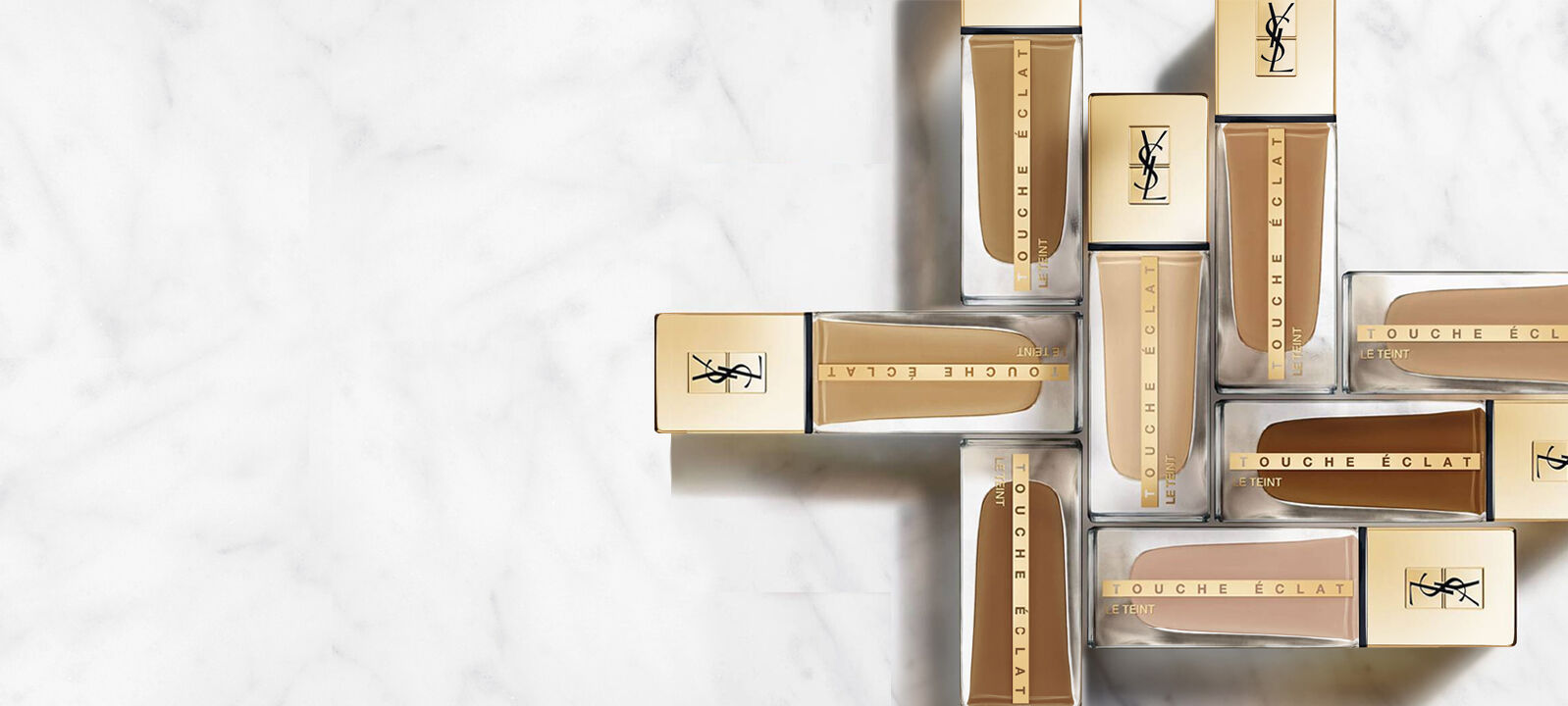 Groupe de flacons de fond de teint Touche Eclat de Yves Saint Laurent sur un fond marbre.