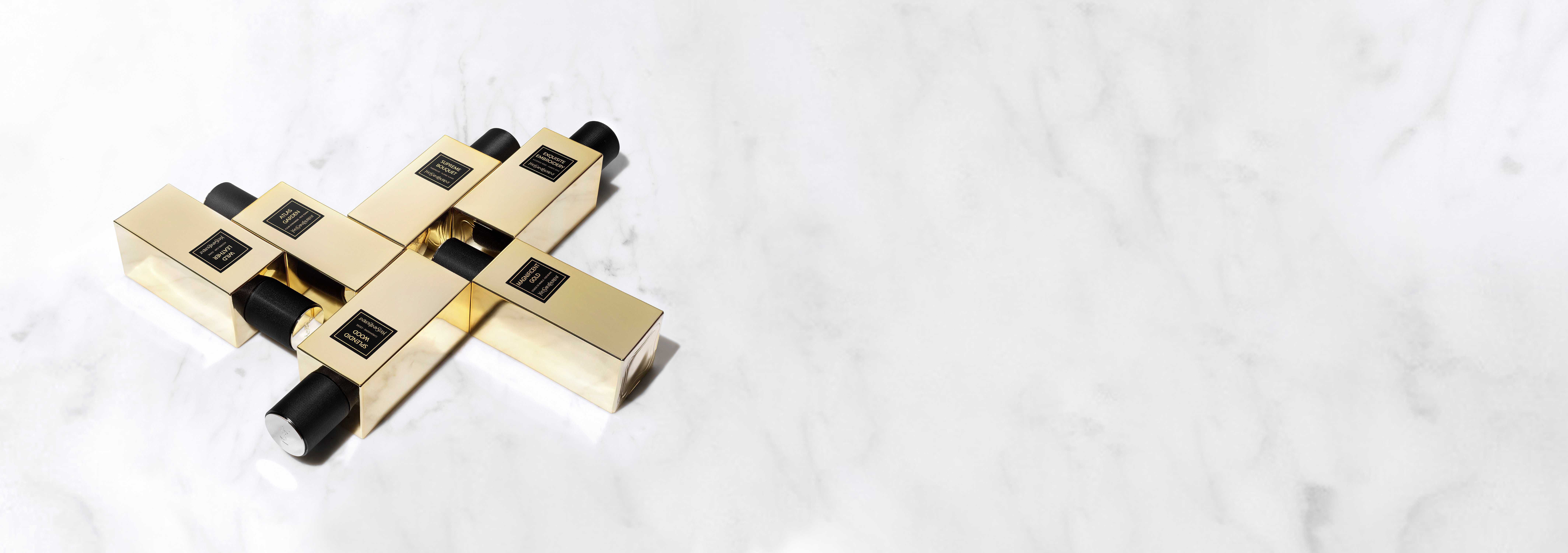 Des flacons de parfum elegants en or sur une surface en marbre, disposes en croix.