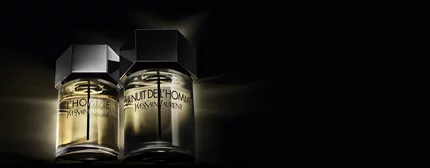 Deux flacons de parfum "L'Homme" de Yves Saint Laurent, l'un a cote de l'autre, sur fond noir avec un eclairage subtil, mettant en valeur leur elegance.
