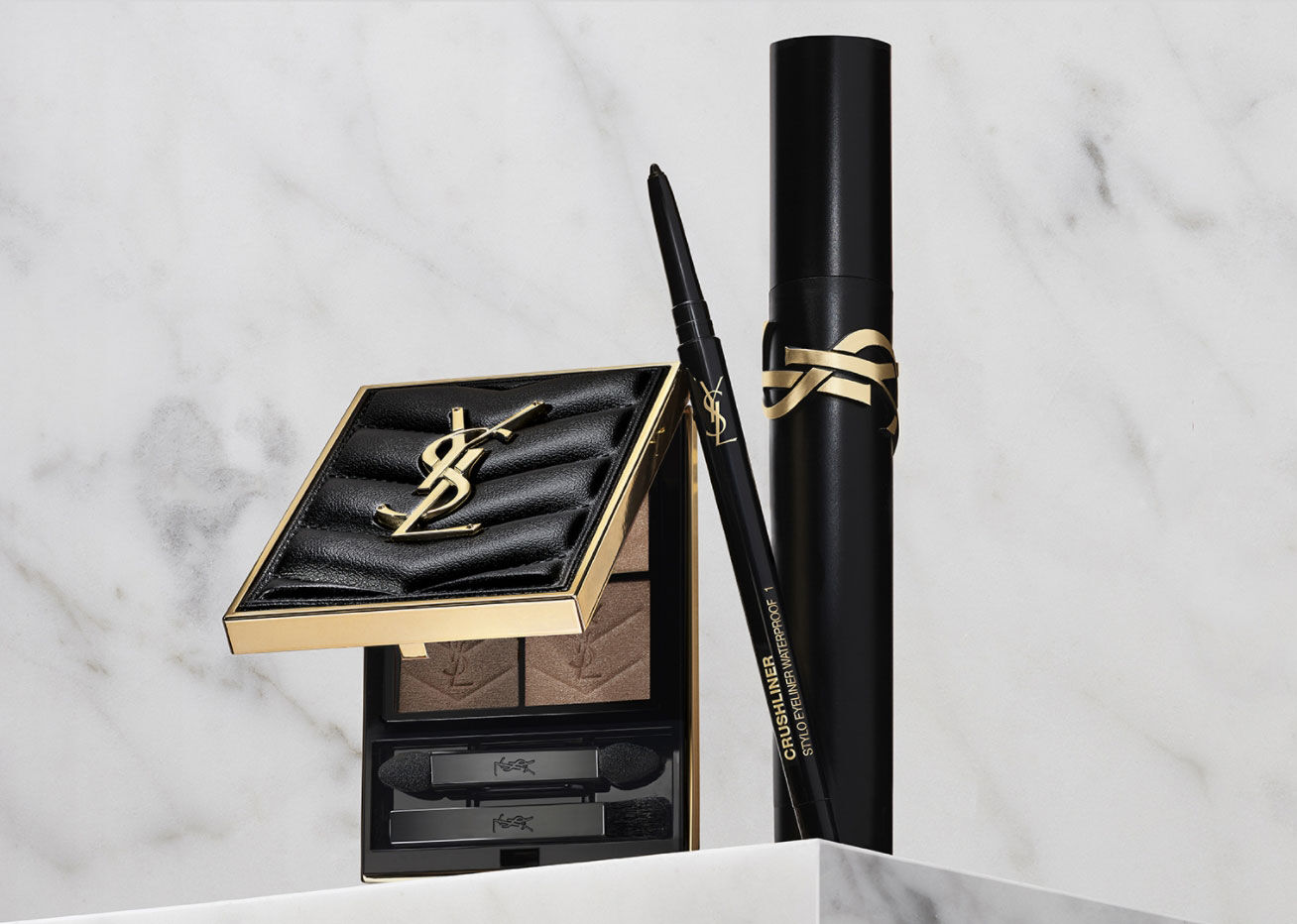 Un produit de maquillage YSL avec une palette de fards a paupieres, un eyeliner et un mascara, poses sur une surface marbree.