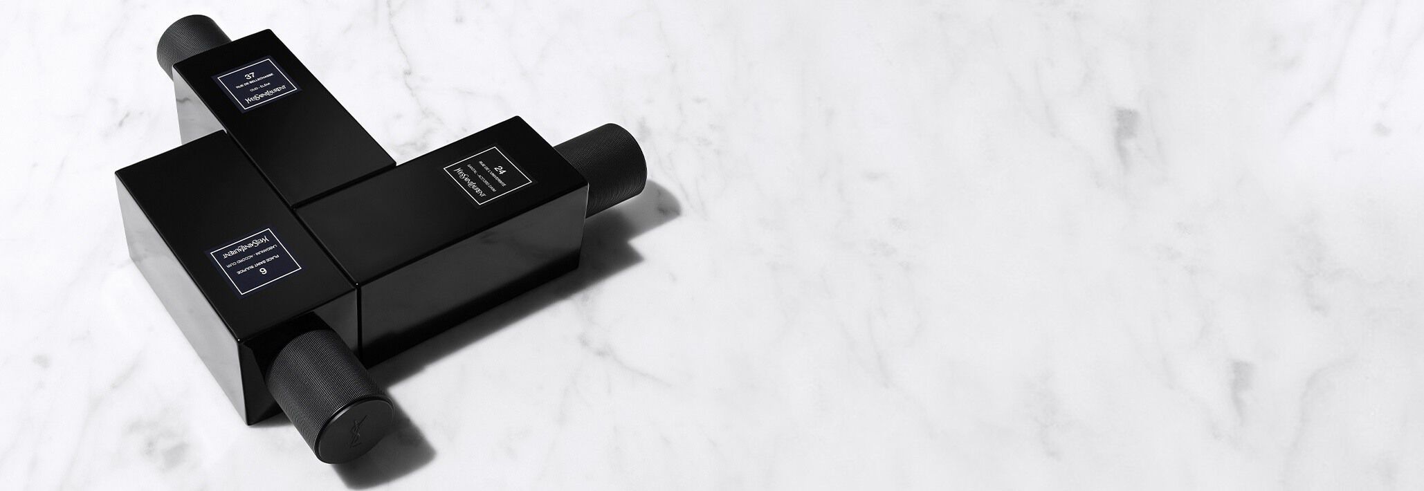 Trois flacons noirs contenant du parfum, disposes en croix sur une surface en marbre blanc.