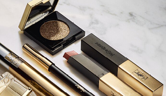 Produits de maquillage et parfum avec des emballages dores, disposes sur une surface brillante.