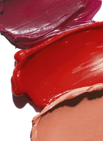 Des echantillons de rouges a levres en differentes teintes : violet, rouge vif et nude, appliques en traits sur une surface.