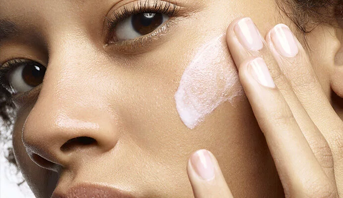 Une femme appliquant une creme sur son visage, avec une expression concentree.