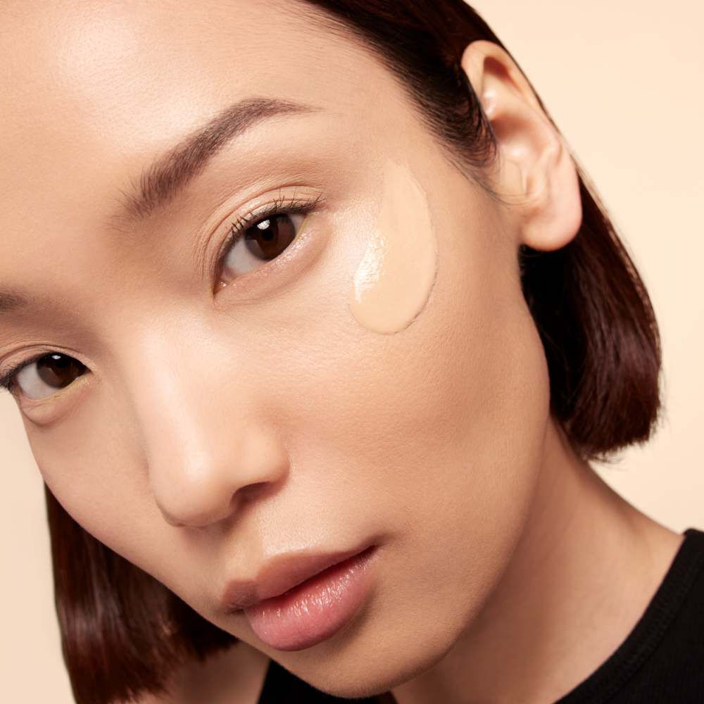 A close-up of a woman applying foundation on her cheek, showcasing her smooth skin and natural makeup look.