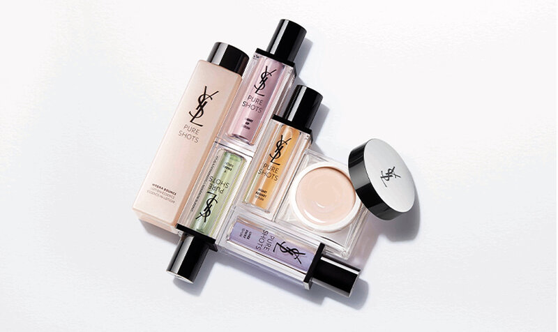 A flat lay of various YSL beauty products, including foundations, serums, and creams, arranged artistically on a clean, light background.