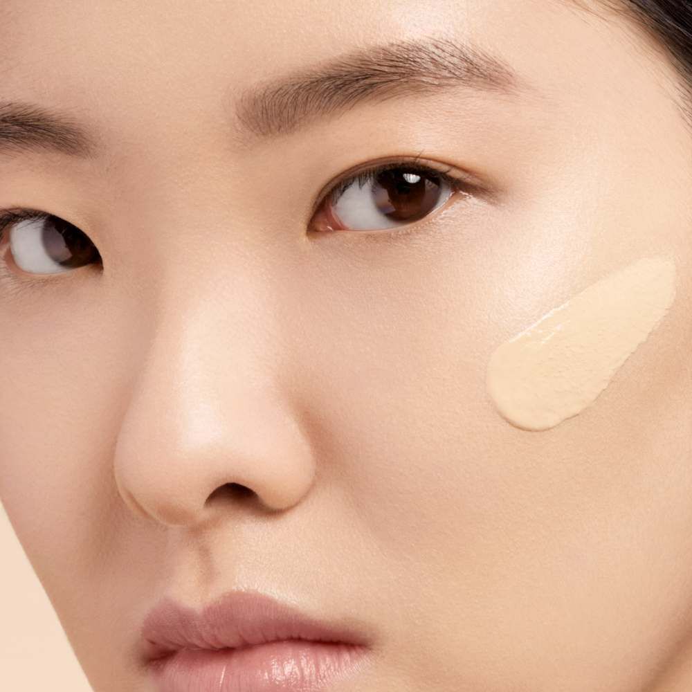 Close-up of a woman's face with a stroke of foundation on her cheek, highlighting her skin texture and natural beauty.