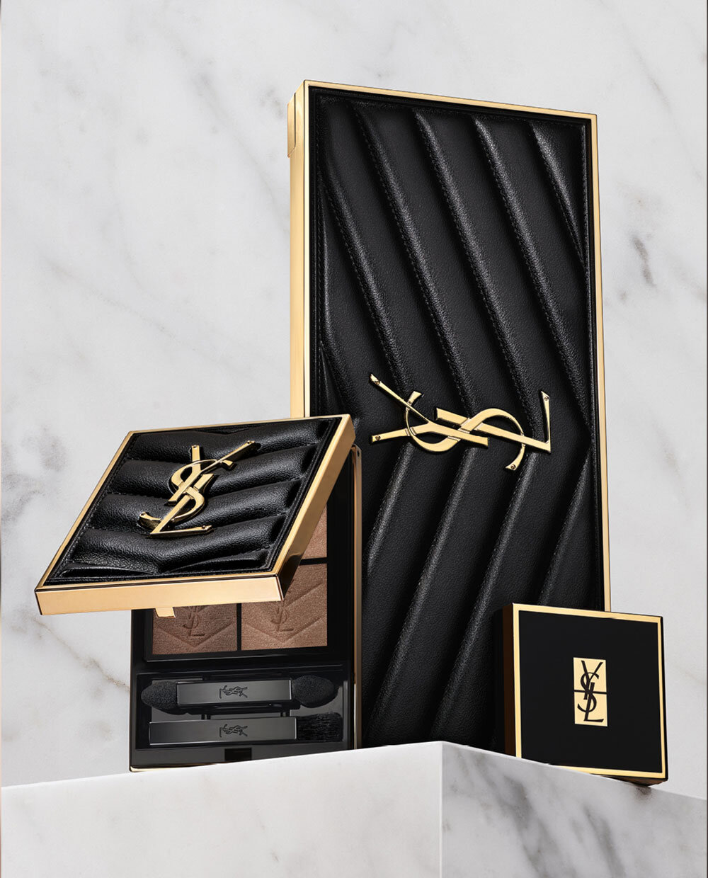 Texte alternatif : Produits de maquillage de luxe YSL presentes sur un fond en marbre, incluant une palette et des poudres compacts.