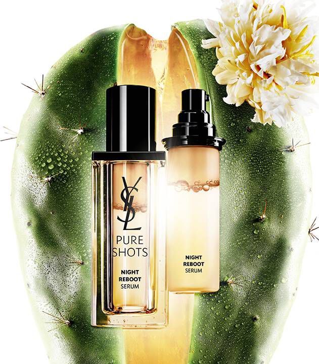 Un flacon de serum de nuit sur un fond de cactus avec une fleur, mettant en avant le produit "Pure Shots Night Reboot Serum" de YSL.