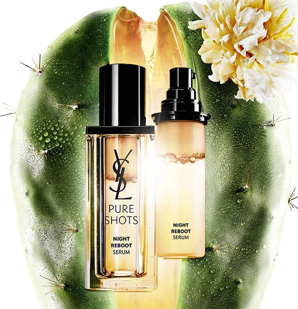 Un flacon de serum de nuit sur un fond de cactus avec une fleur, mettant en avant le produit "Pure Shots Night Reboot Serum" de YSL.