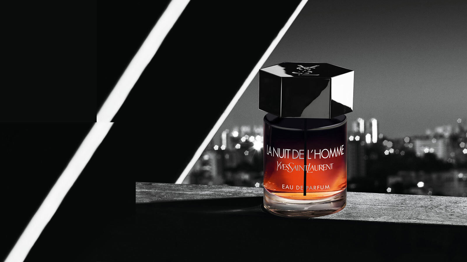 Flacon de parfum "La Nuit de l'Homme" d'Yves Saint Laurent, presente sur un fond urbain nocturne.