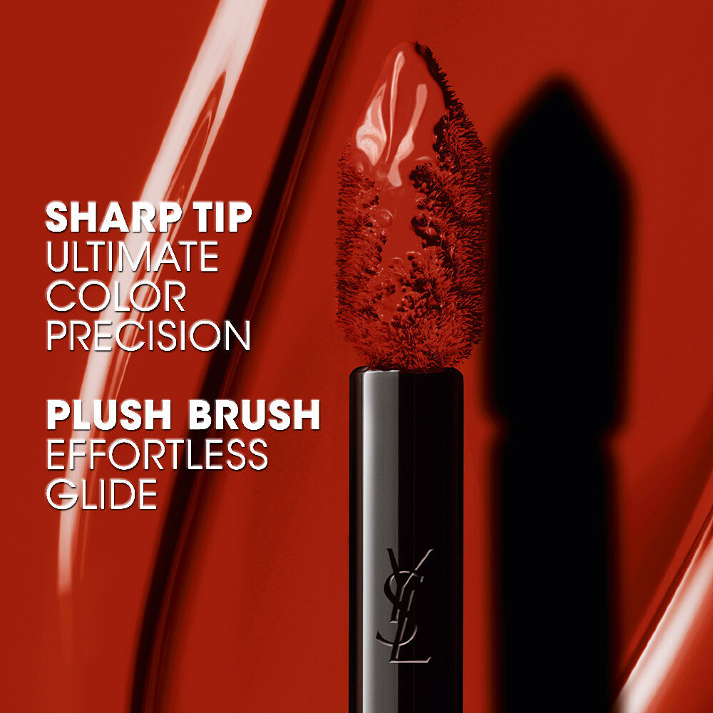 Gros plan sur un pinceau-applicateur YSL a pointe aiguisee, enduit d’un rouge liquide brillant. Le texte s’affiche : *« PRECISION COULEUR EXTREME POINTE AIGUE »* et *« GLISSE INSTANTANEE POUSSIERE SOYEUSE »*.