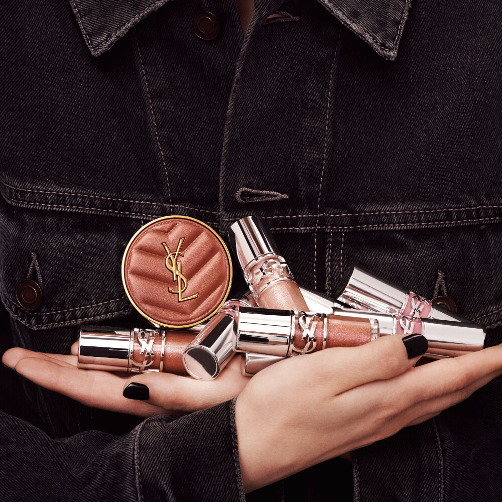 Hands holding YSL LOVESHINE Plumping Lip Oil Gloss and Make Me Blush, showcasing luxury beauty products.