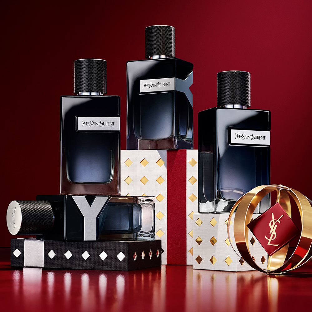 Des flacons YSL Y Eau de Parfum empiles sur des ecrins de fete noirs, blancs et dores.