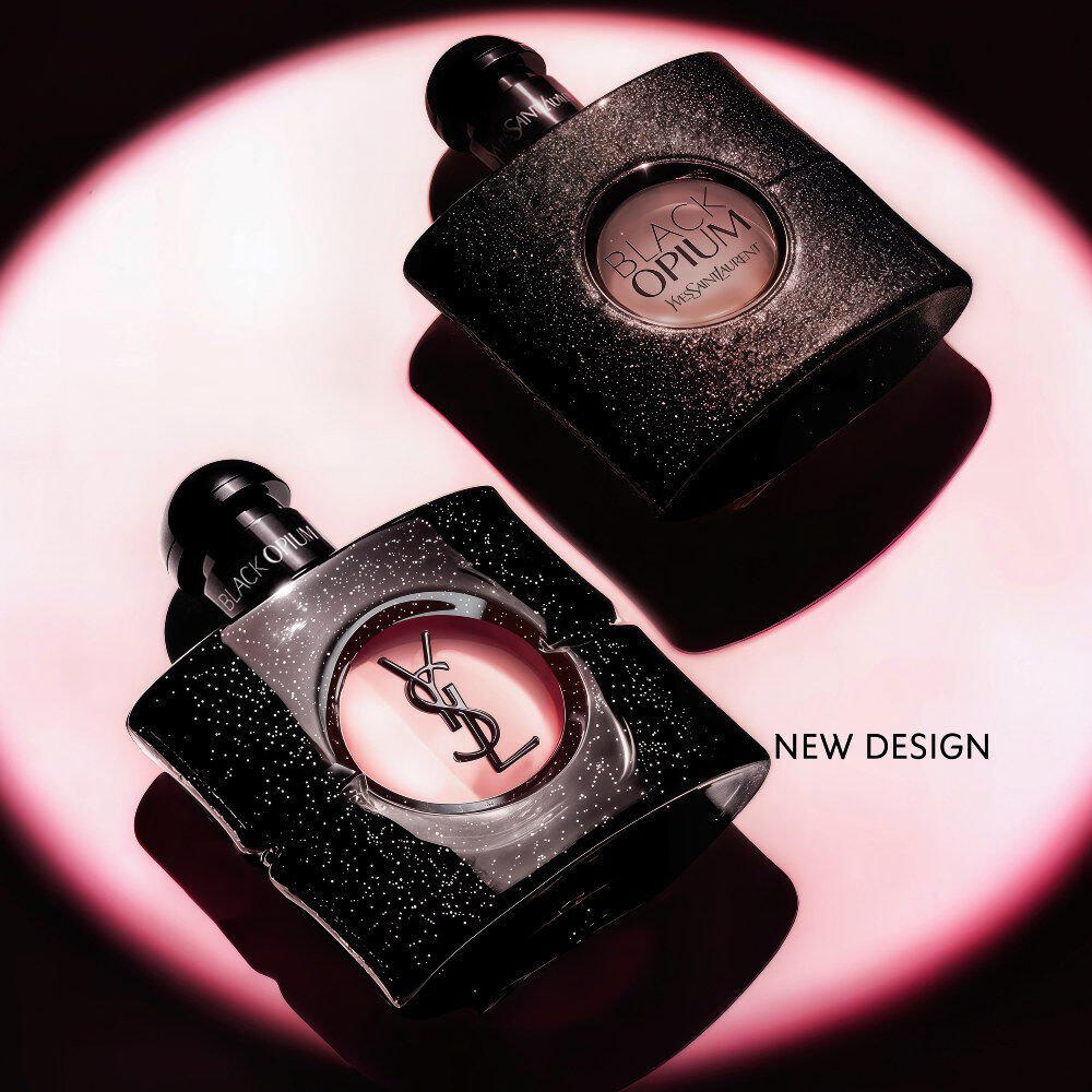 Flacon de Black Opium Eau de Parfum pose sur le cote sur une surface sombre, aureole d’une lumiere rose.