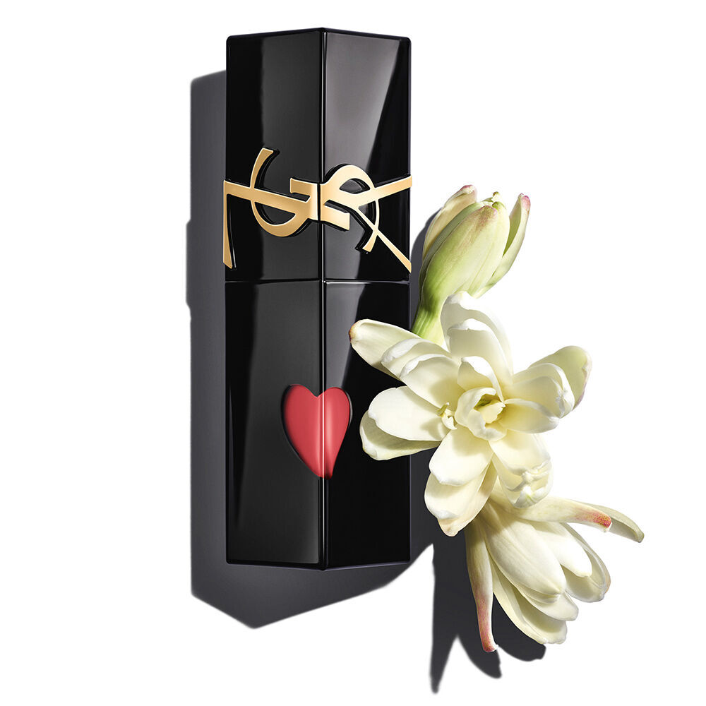 Un flacon de teinture a levres YSL noir brillant, decoupe d’un coeur rouge, expose avec elegance aux cotes de tubereuses blanches en pleine floraison.
